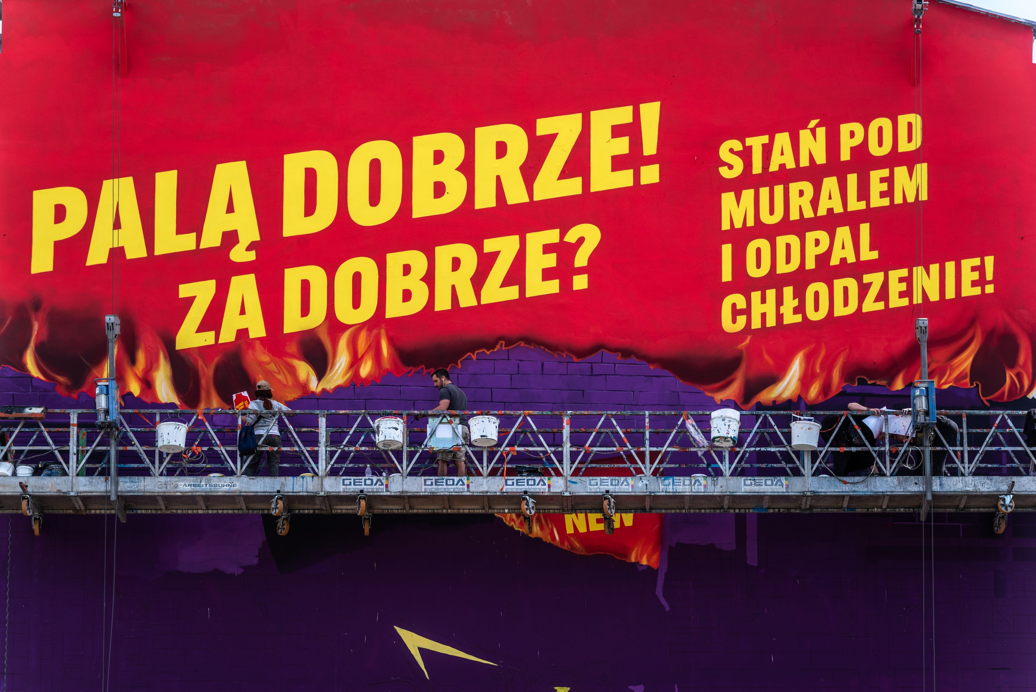 malarze na windzie malują mural Lays